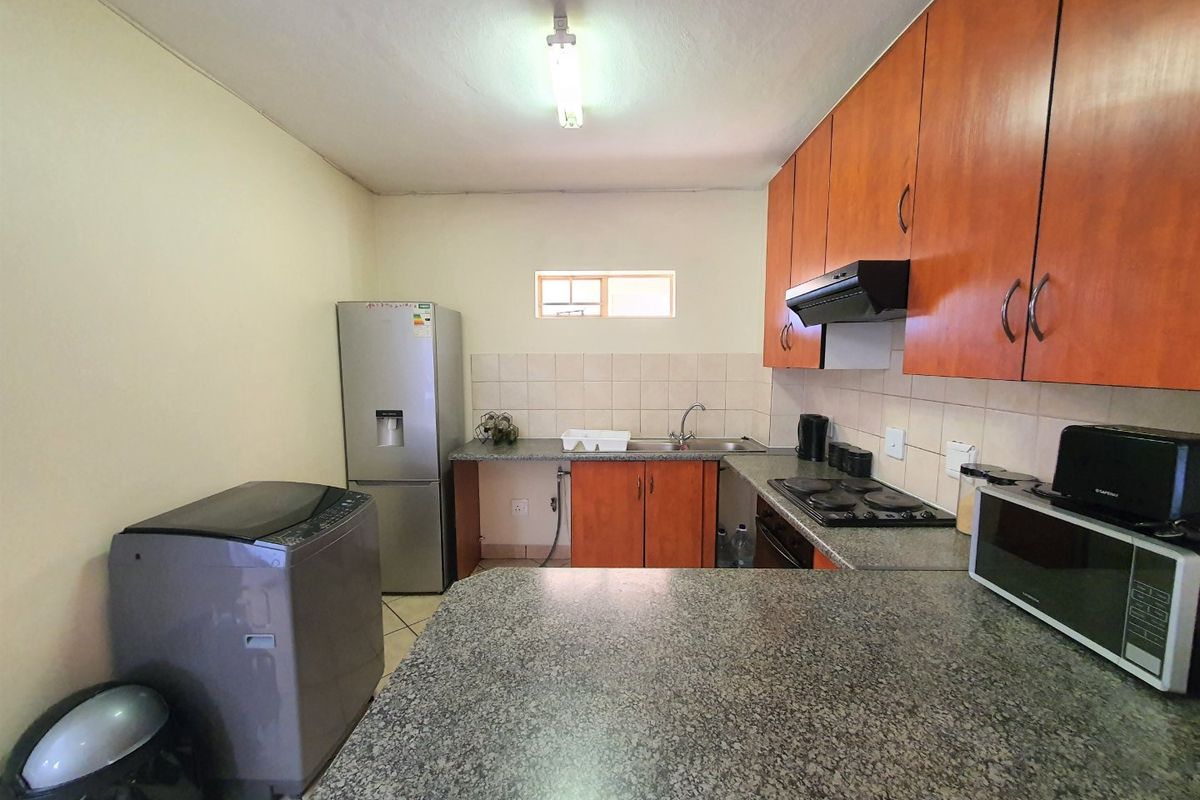 Functional kitchen featuring wood-finish cabinetry, granite countertops, tiled backsplash, and built-in electric hob with extractor fan.