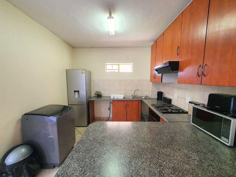 Functional kitchen featuring wood-finish cabinetry, granite countertops, tiled backsplash, and built-in electric hob with extractor fan.