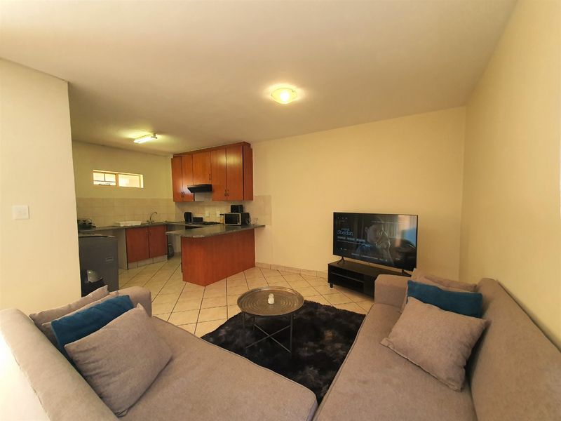 Open-plan living area featuring a functional kitchen with wood-finish cabinetry, granite countertops, and tiled flooring throughout the combined space.