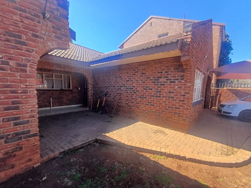 A rear exterior view of a face brick townhouse featuring a paved patio area and a covered archway entrance.