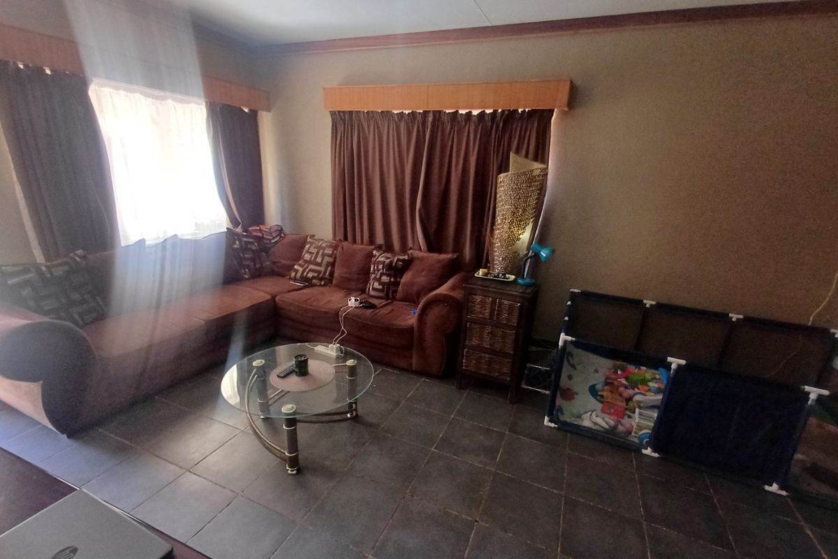 A living room featuring dark floor tiles and window pelmets, offering a functional space that could benefit from modern updates.