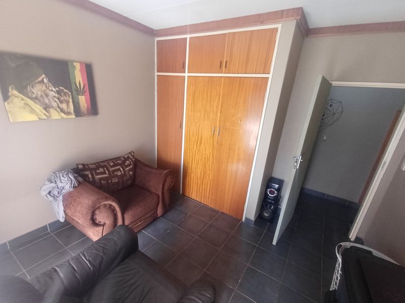 A bedroom featuring built-in wooden cupboards, tiled flooring, and crown molding, offering a functional space with potential for cosmetic updates.