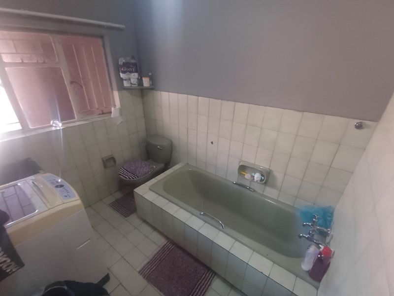 A dated bathroom featuring a built-in bathtub, toilet, and tiled finishes, offering potential for modernization and renovation.