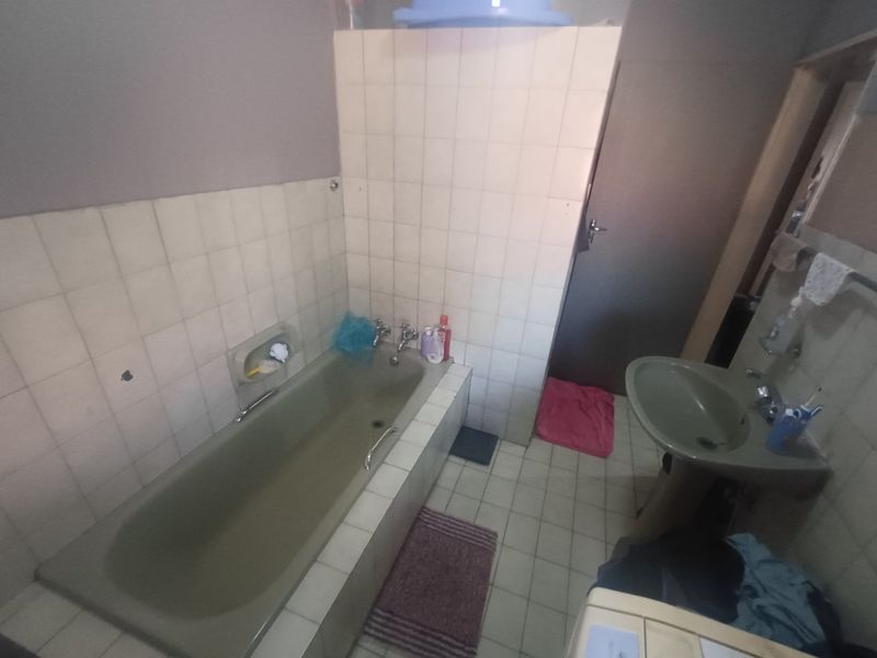 A dated bathroom featuring a built-in bathtub and pedestal basin with tiled finishes, requiring cosmetic updates to modernize the space.