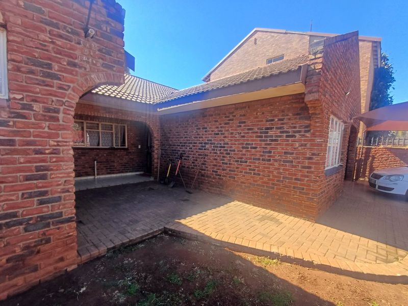 Rear view of a face brick townhouse featuring a paved patio area, arched architectural details, and a tiled roof.