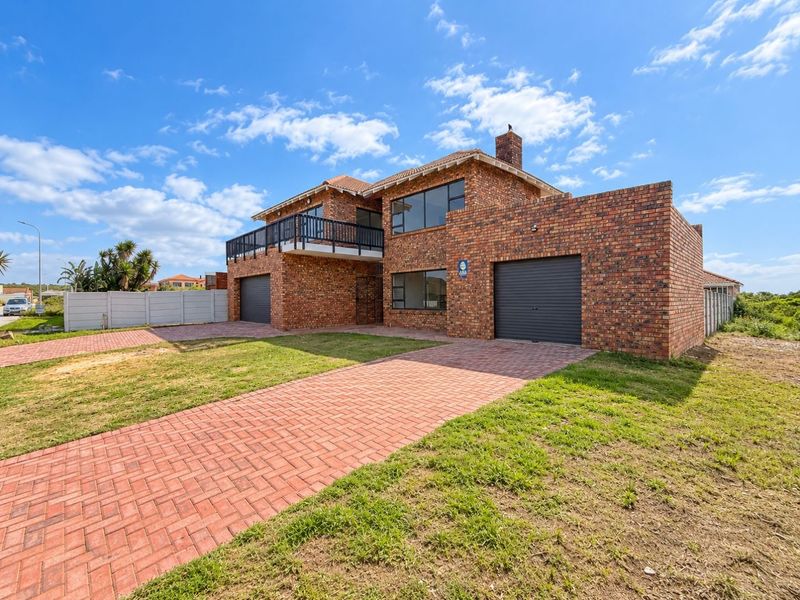 A double-story face brick house featuring a double garage, a balcony, and a paved driveway set on a landscaped plot.
