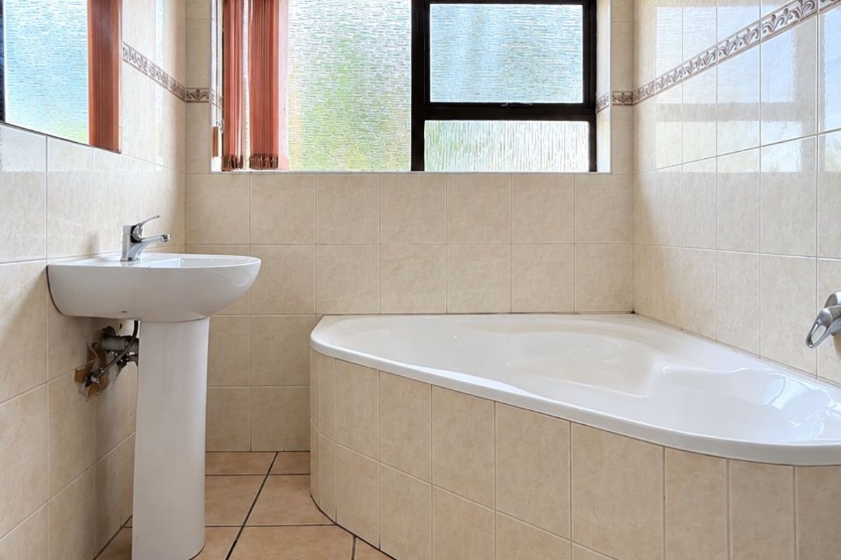 A functional bathroom featuring a corner bathtub, pedestal basin, and neutral floor-to-ceiling wall tiling.