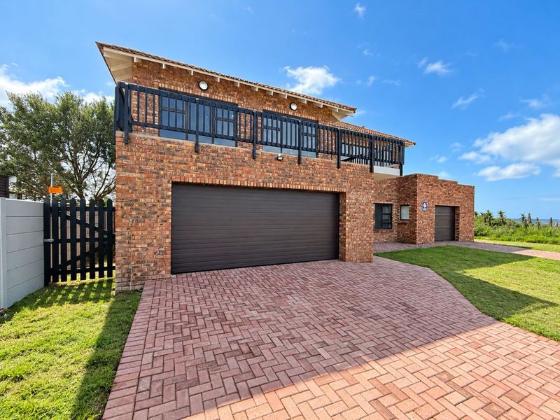 A modern double-story brick house featuring a paved driveway, multiple garage doors, and an upper-level balcony with a black railing.