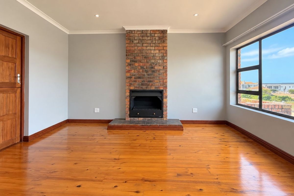 Spacious living room featuring polished timber flooring, a central brick fireplace, and large windows providing natural light and exterior views.