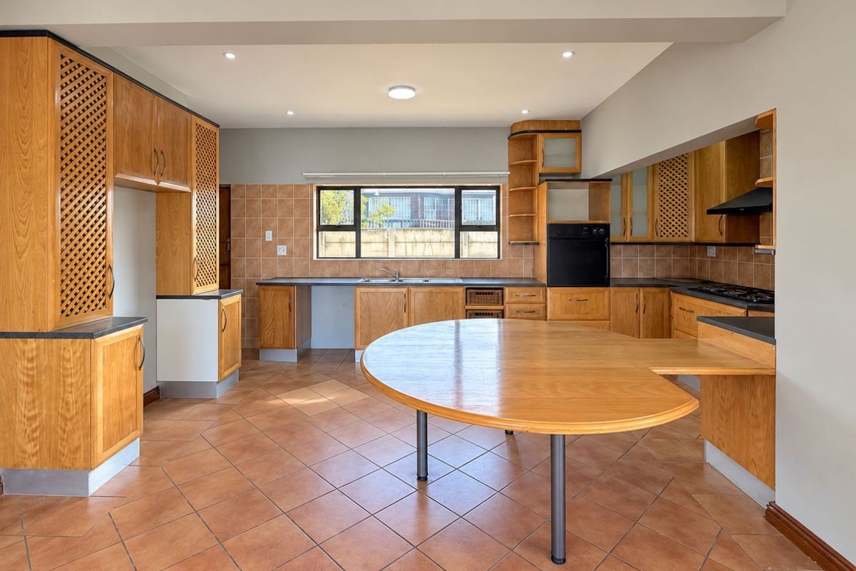 Spacious kitchen featuring extensive wooden cabinetry, built-in oven, gas hob, and a large integrated breakfast counter with tiled flooring throughout.