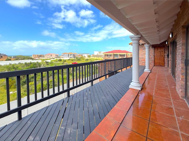 Spacious covered balcony featuring terracotta tiling, timber decking, and decorative columns, offering an elevated outdoor space with scenic neighbourhood views.