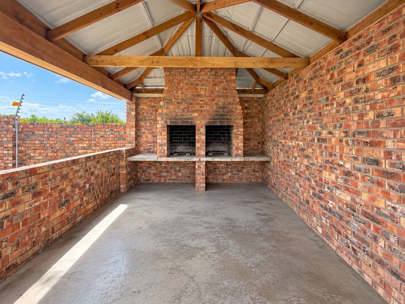 Covered outdoor patio featuring a double built-in brick braai, exposed timber roof trusses, and durable concrete flooring, ideal for outdoor entertaining.