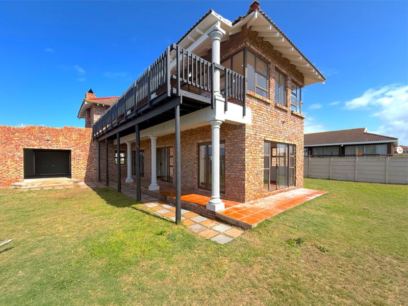Rear view of a double-story brick house featuring a spacious balcony, covered patio area, and attached garage set within a private garden.