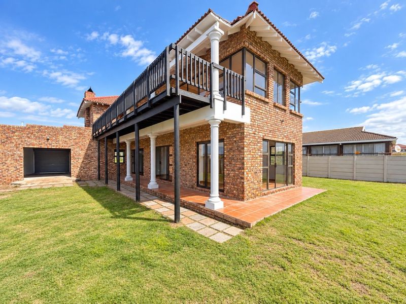 A well-maintained double-story face brick home featuring a spacious covered patio, an upper-level balcony with classical columns, and an attached garage.