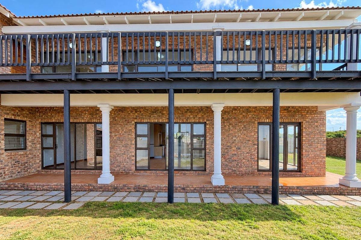 A well-maintained rear exterior view featuring an exposed brick facade, a spacious ground-floor tiled patio, and an expansive upper-level balcony with dark railings.