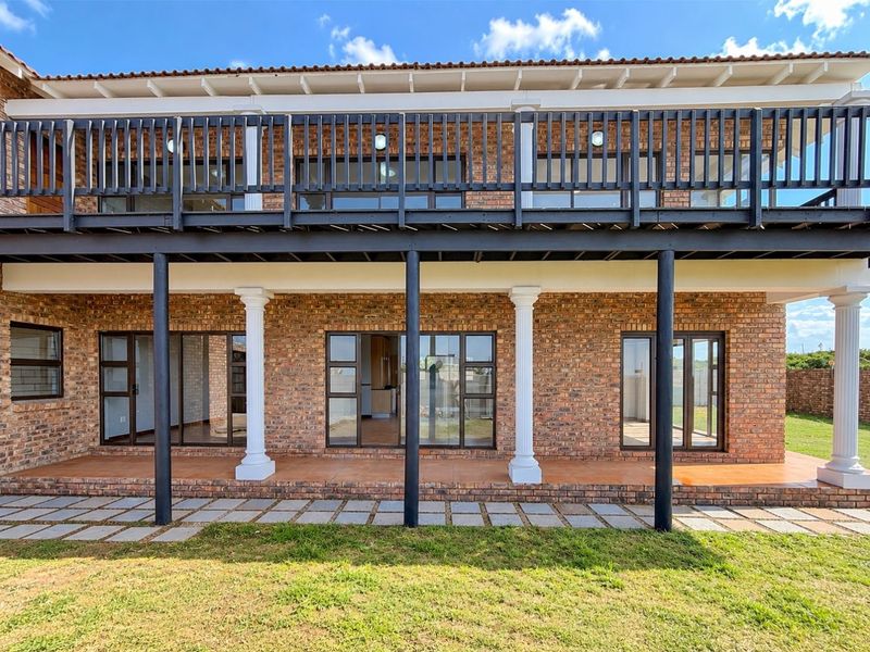 A well-maintained rear exterior view featuring an exposed brick facade, a spacious ground-floor tiled patio, and an expansive upper-level balcony with dark railings.
