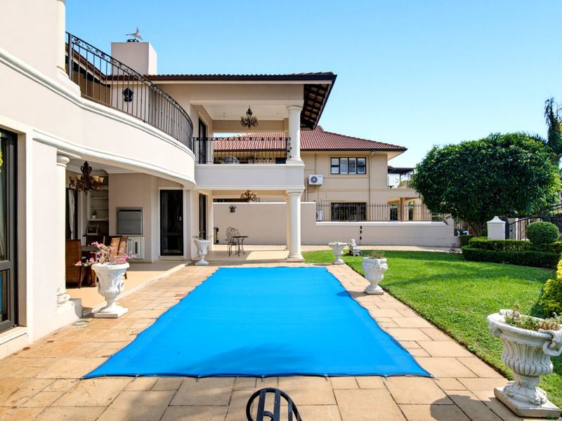 Spacious outdoor entertainment area featuring a covered patio, balcony, and a swimming pool with a safety cover, set within a well-maintained garden.