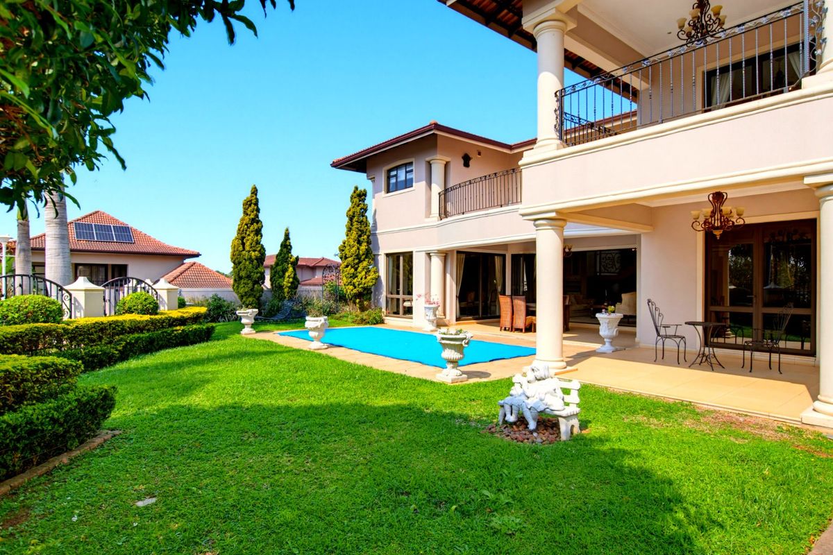 Spacious rear exterior featuring a covered patio, upper balcony with wrought iron railings, swimming pool, and well-maintained landscaped garden.