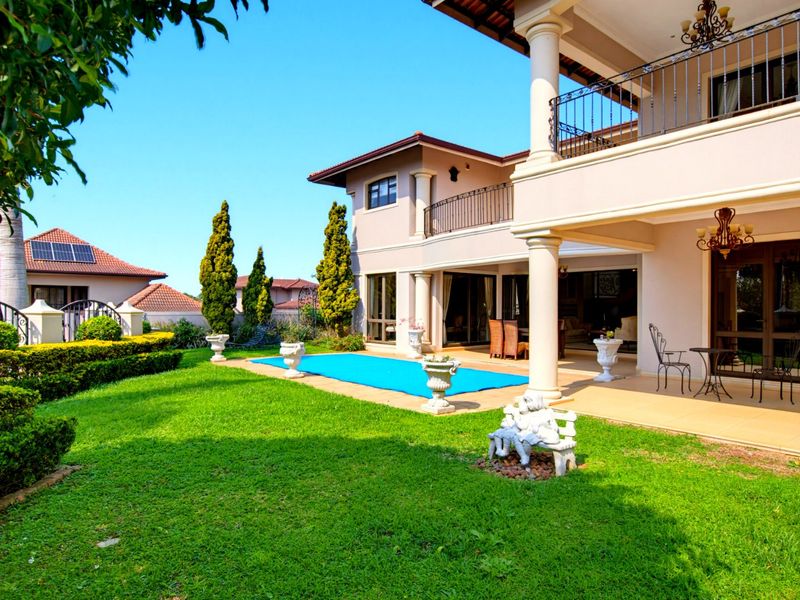 Spacious rear exterior featuring a covered patio, upper balcony with wrought iron railings, swimming pool, and well-maintained landscaped garden.