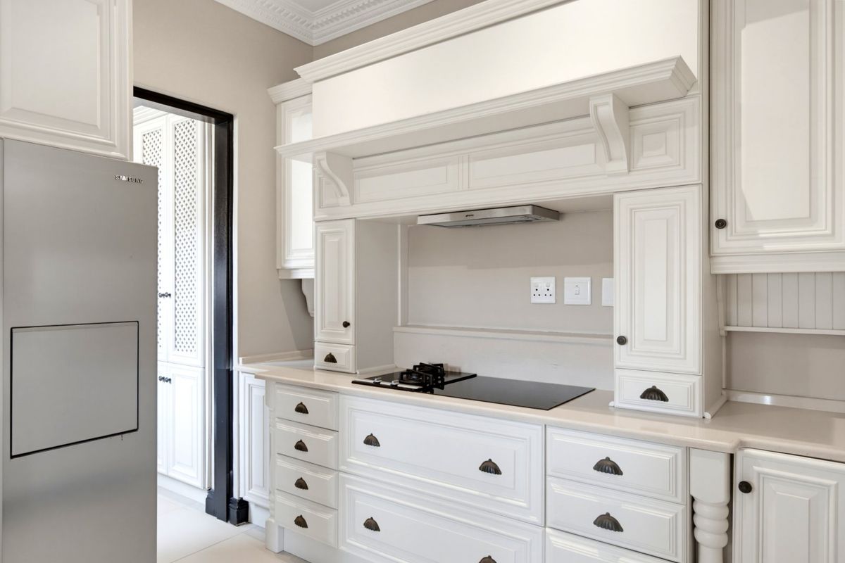 A well-appointed kitchen featuring classic white cabinetry, stone countertops, a built-in gas hob with extractor fan, and elegant crown molding details.