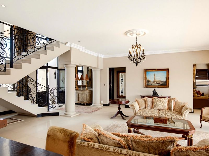 Spacious living area featuring a grand stone staircase with ornate wrought iron railings, classical columns, and elegant crown molding.