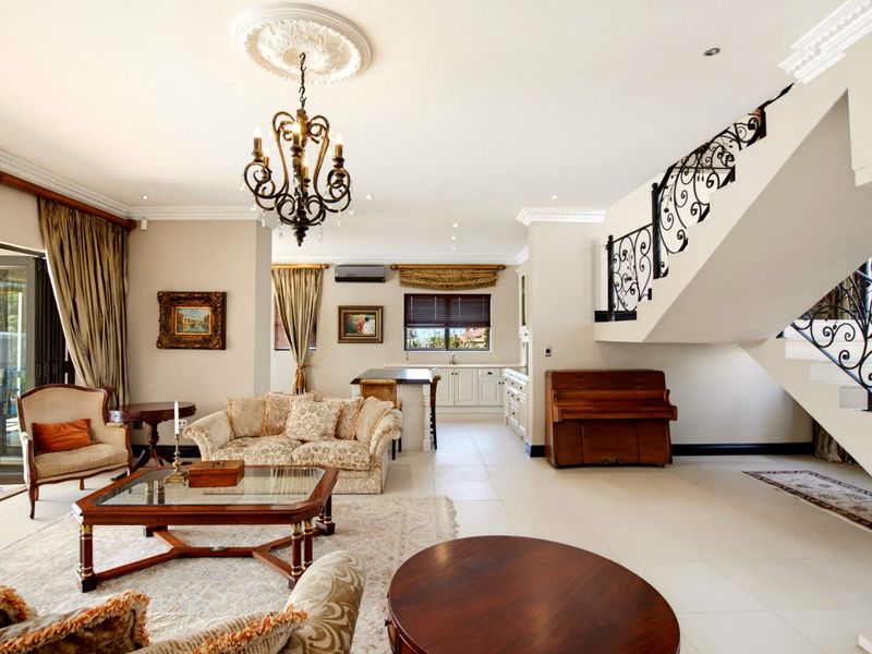 Spacious open-plan living area featuring tiled floors, a decorative wrought iron staircase, and a seamless transition to the kitchen and outdoor patio.