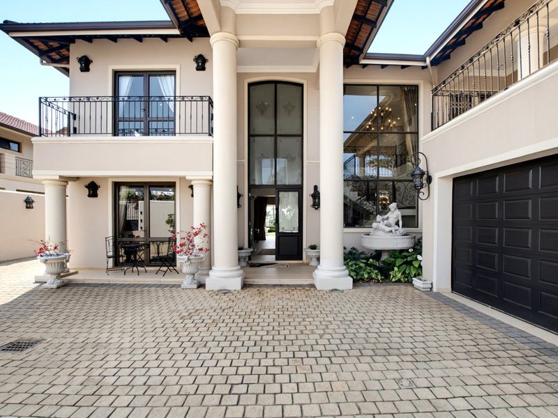 Impressive double-story front facade featuring grand columns, a paved driveway, double garage, and elegant wrought iron balcony detailing.