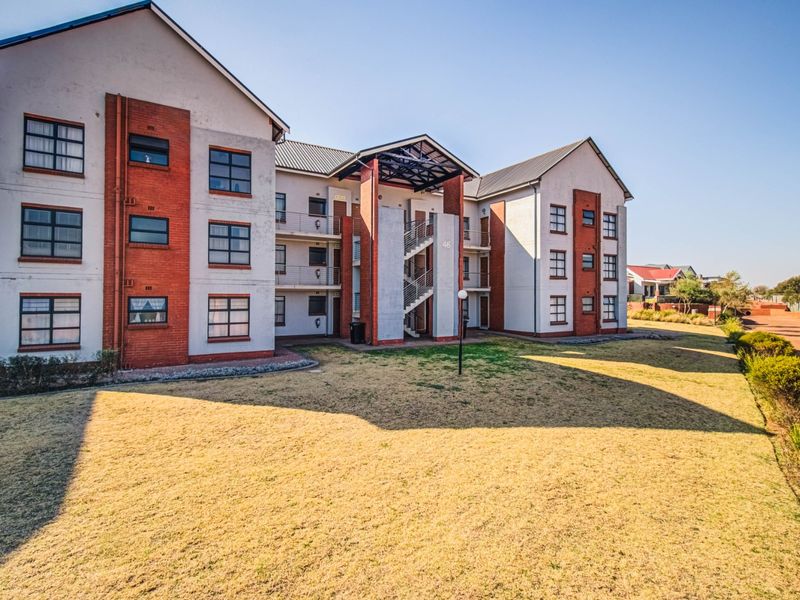 Exterior view of a multi-story apartment complex featuring brick and plaster facade with an open-air staircase and surrounding landscaped grounds.