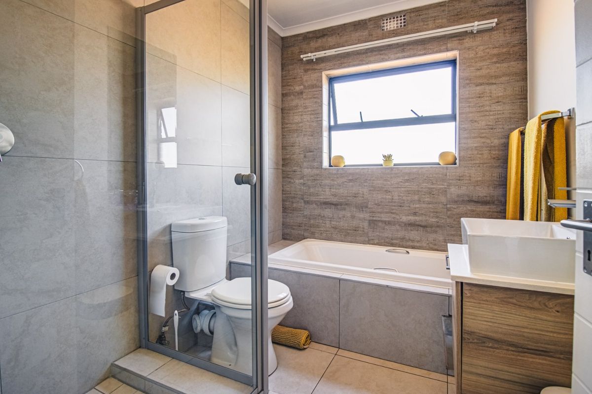 Modern bathroom featuring a glass-enclosed shower, a built-in bathtub, a vanity basin, and neutral-toned wall and floor tiling.