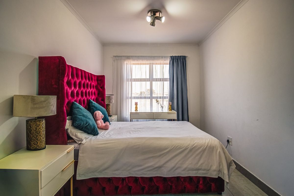 A well-maintained bedroom featuring tiled flooring, neutral walls, and a large window with curtain tracks, providing a bright and comfortable living space.