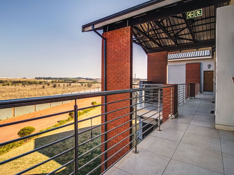 A spacious covered balcony featuring tiled flooring, stainless steel balustrades, and exposed brick pillars, offering expansive views of the surrounding landscape.