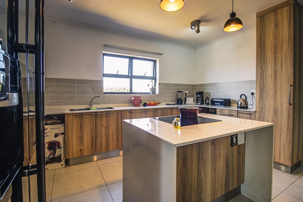Modern kitchen featuring wood-finish cabinetry, stone countertops, a central island with an induction cooktop, and integrated built-in oven.