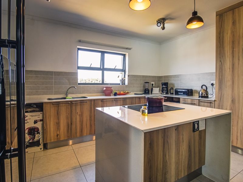 Modern kitchen featuring wood-finish cabinetry, stone countertops, a central island with an induction cooktop, and integrated built-in oven.