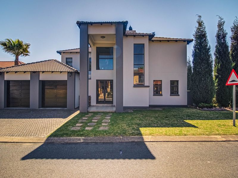 Modern double-storey residential home featuring a double garage, paved driveway, and a striking double-volume entrance facade with large glass windows.