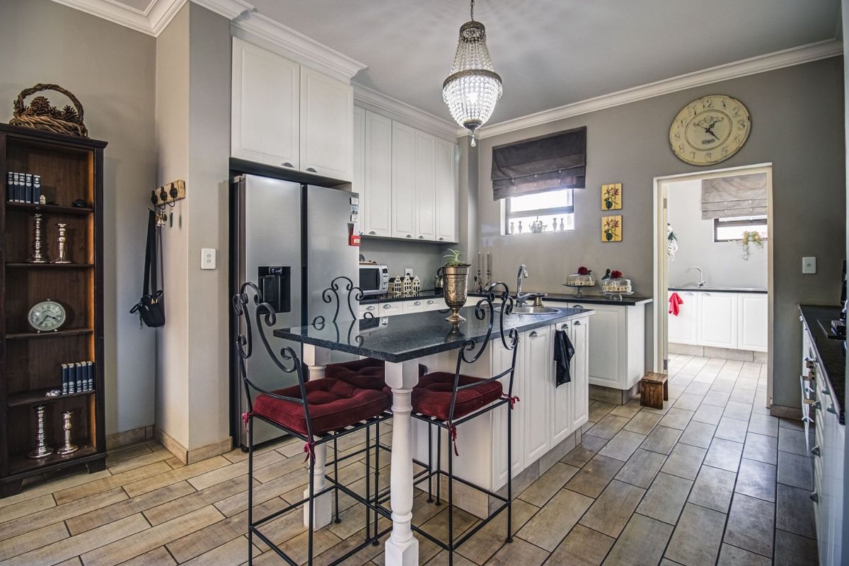 A well-maintained kitchen featuring a central island with granite countertops, white cabinetry, and tiled flooring, with an adjacent scullery visible.
