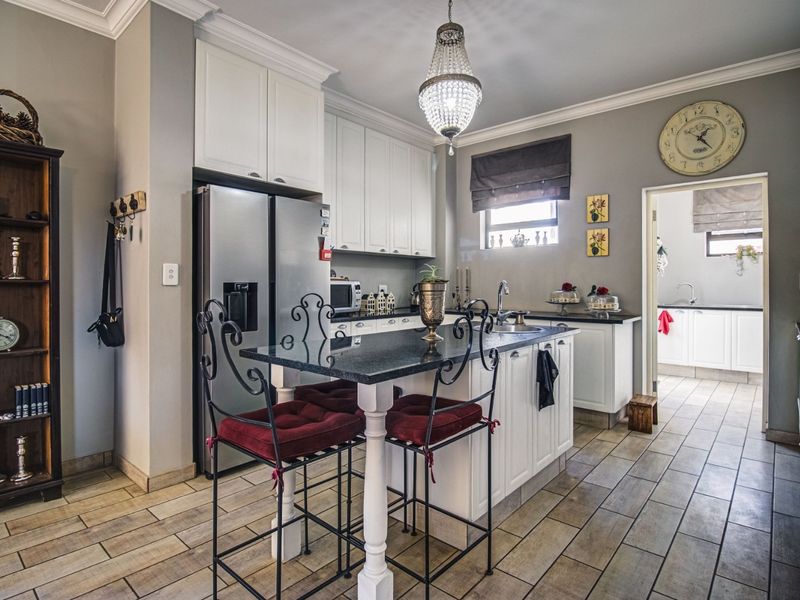 A well-maintained kitchen featuring a central island with granite countertops, white cabinetry, and tiled flooring, with an adjacent scullery visible.