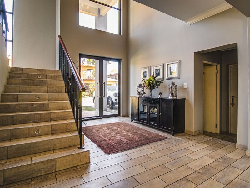 Spacious double-volume entrance hall featuring tiled flooring, a grand staircase with wrought iron balustrade, and large glass doors providing natural light.