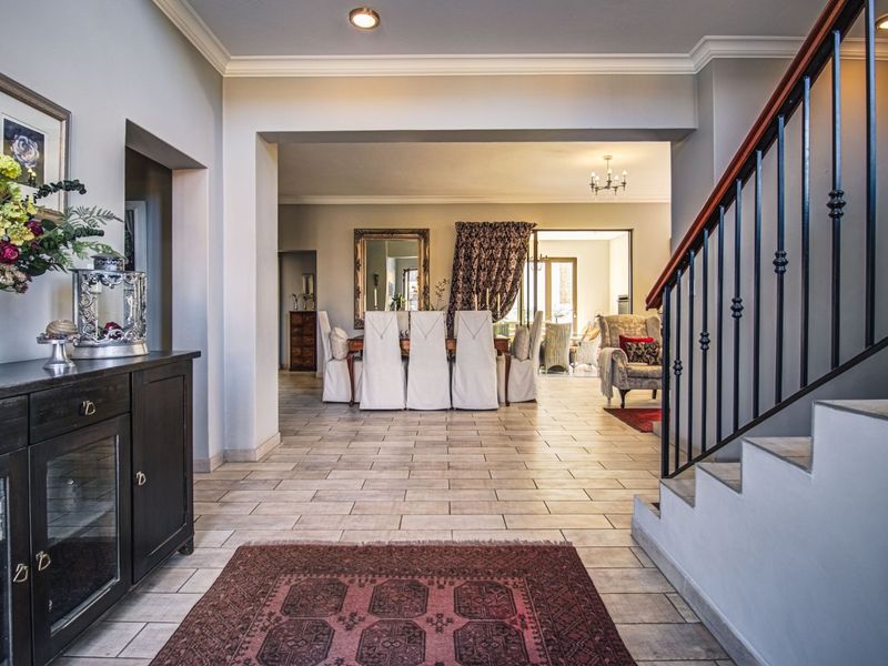 Spacious entrance hall featuring tiled flooring and a staircase with a decorative metal balustrade, leading into an open-plan dining and living area.