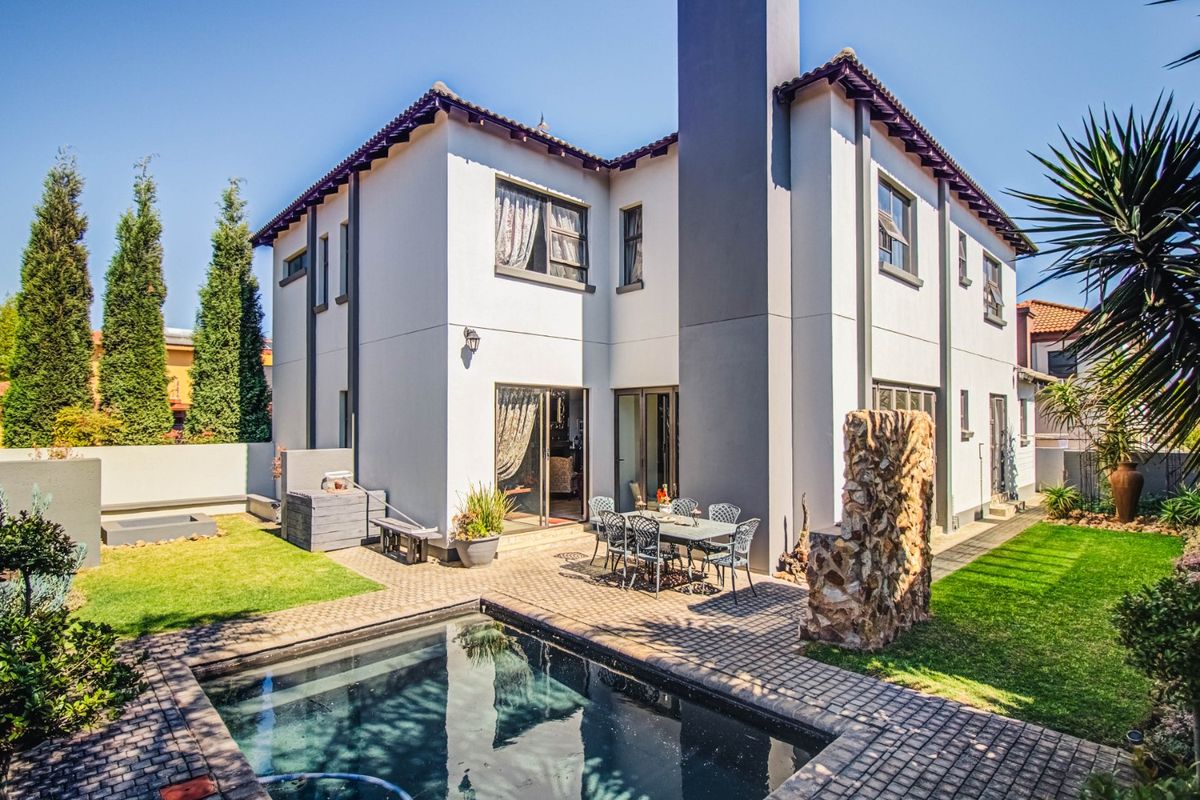 Rear view of the property featuring a paved patio area, a swimming pool, and a well-maintained garden with a prominent chimney stack.