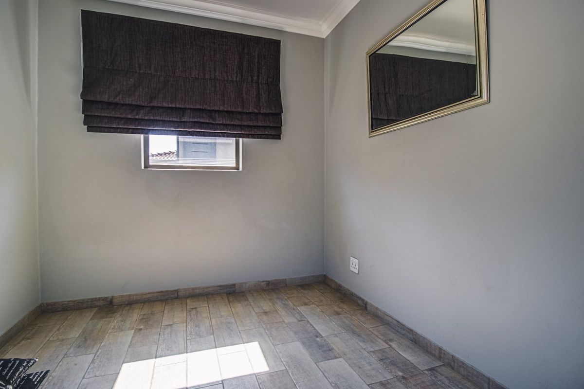 A clean, empty bedroom featuring neutral grey walls, wood-look tiled flooring, and modern coving, providing a versatile space ready for personalization.