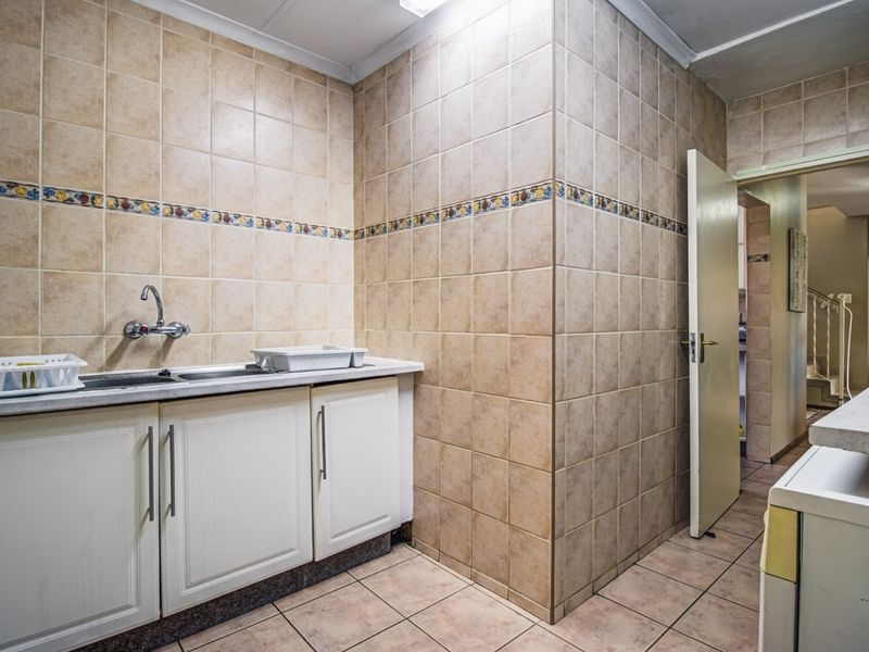 A functional laundry area featuring built-in cabinetry, a stainless steel sink, and full-height ceramic wall tiling.