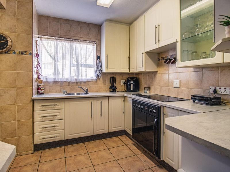 A functional kitchen featuring cream cabinetry, tiled backsplash, ceramic flooring, and integrated appliances including an electric hob and oven.