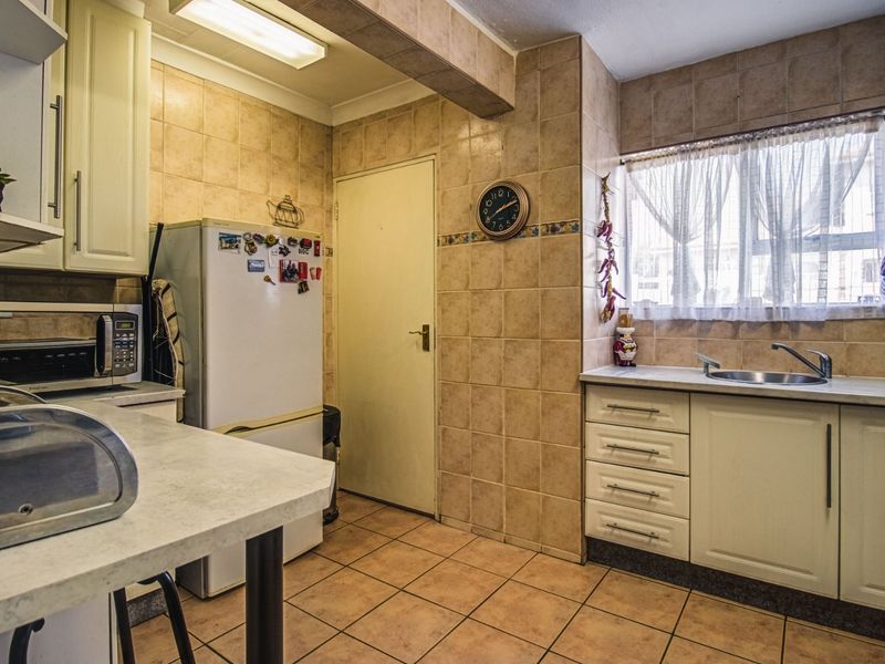 A functional kitchen featuring tiled walls and flooring, ample cabinetry, laminate countertops, and a built-in microwave, offering a practical layout for daily use.