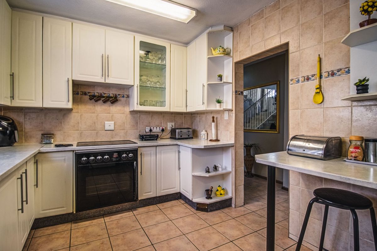 A functional kitchen featuring white cabinetry, tiled backsplash, and a built-in electric oven and hob, with an adjacent breakfast counter area.