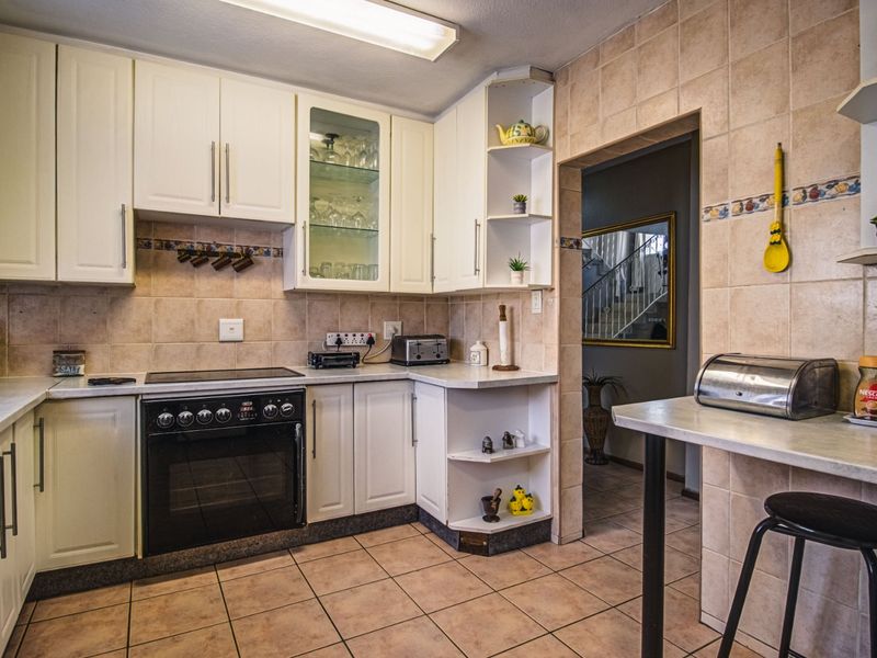A functional kitchen featuring white cabinetry, tiled backsplash, and a built-in electric oven and hob, with an adjacent breakfast counter area.