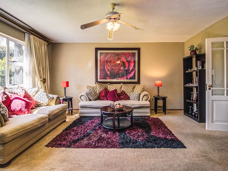 A comfortable living room featuring a ceiling fan, large window for natural light, and a classic panelled door.