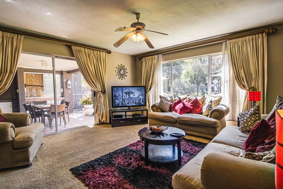 A spacious living room featuring a ceiling fan, large windows for natural light, and sliding glass doors providing access to an outdoor patio area.