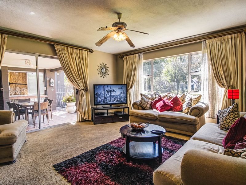 A spacious living room featuring a ceiling fan, large windows for natural light, and sliding glass doors providing access to an outdoor patio area.