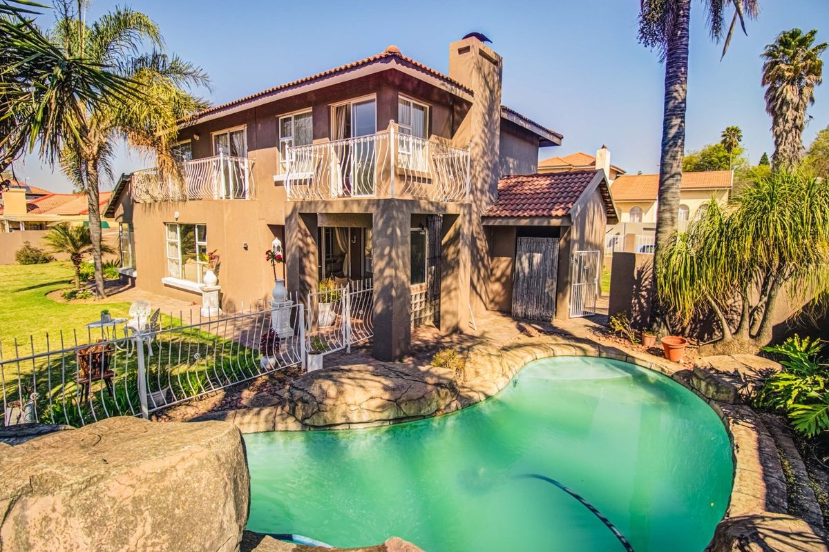 Rear view of the property featuring a landscaped garden, a rock-surround swimming pool, and an upper-level balcony with wrought iron railings.