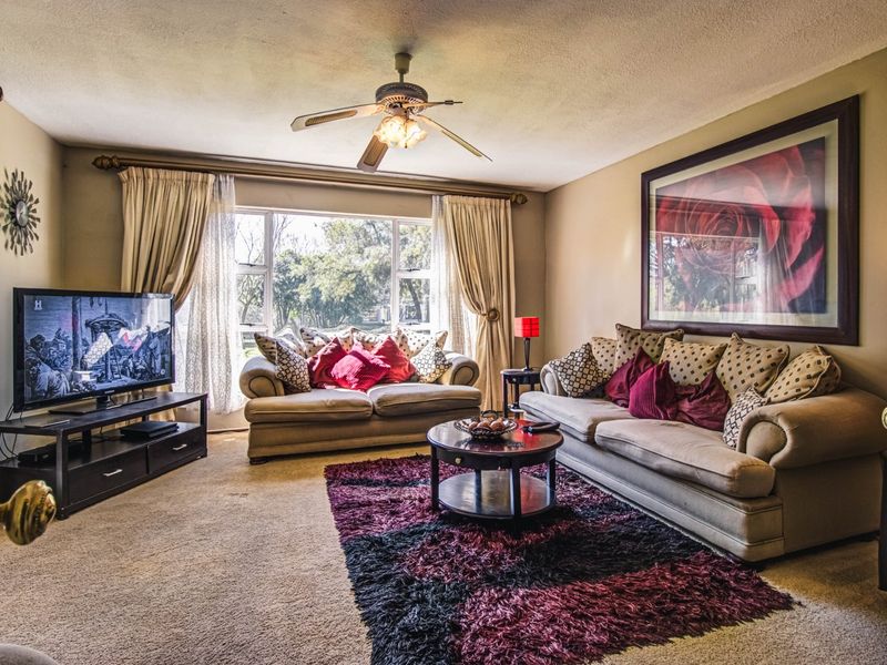 A comfortable living room featuring a ceiling fan, large window for natural light, and neutral wall tones.